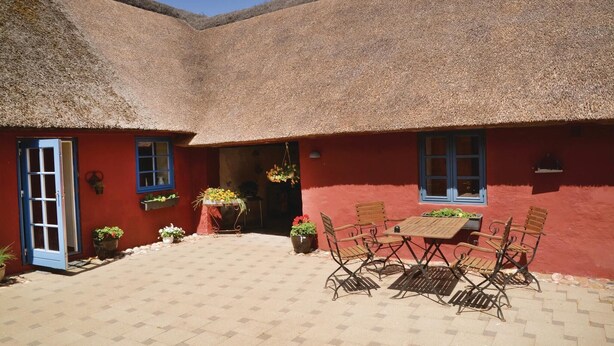 Een rood gebouw met rieten dak en een klein terras met een tafel en stoelen.