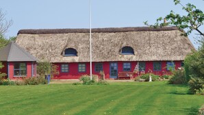 Een traditioneel rieten huis met een rode gevel en een klein aangrenzend gebouw met een grijs dak.