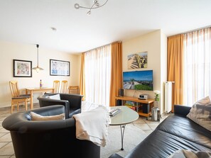 A living room with a sofa, a coffee table, and a TV. There is a dining area with chairs and a table.