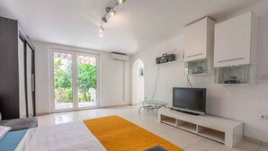 Ein modernes Schlafzimmer mit Bett, Fernseher auf einem Schrank und Balkon mit Blick ins Grüne.