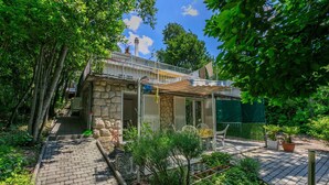 Ein Steinhaus mit einer überdachten Terrasse, umgeben von üppiger Vegetation und Bäumen.