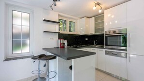 Eine moderne Küche mit weißen Schränken, einer zentralen Kochinsel mit Barhocker, einer Kaffeemaschine und Blick aus dem Fenster.