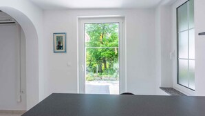 Ein modernes Zimmer mit dunkelgrauem Tresen, einer weißen Tür, die in einen Garten führt, und einem gerahmten Bild an der Wand.