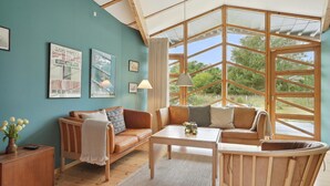 Une pièce chaleureuse avec une grande fenêtre, un plafond en bois, un canapé, une table basse et un petit meuble.