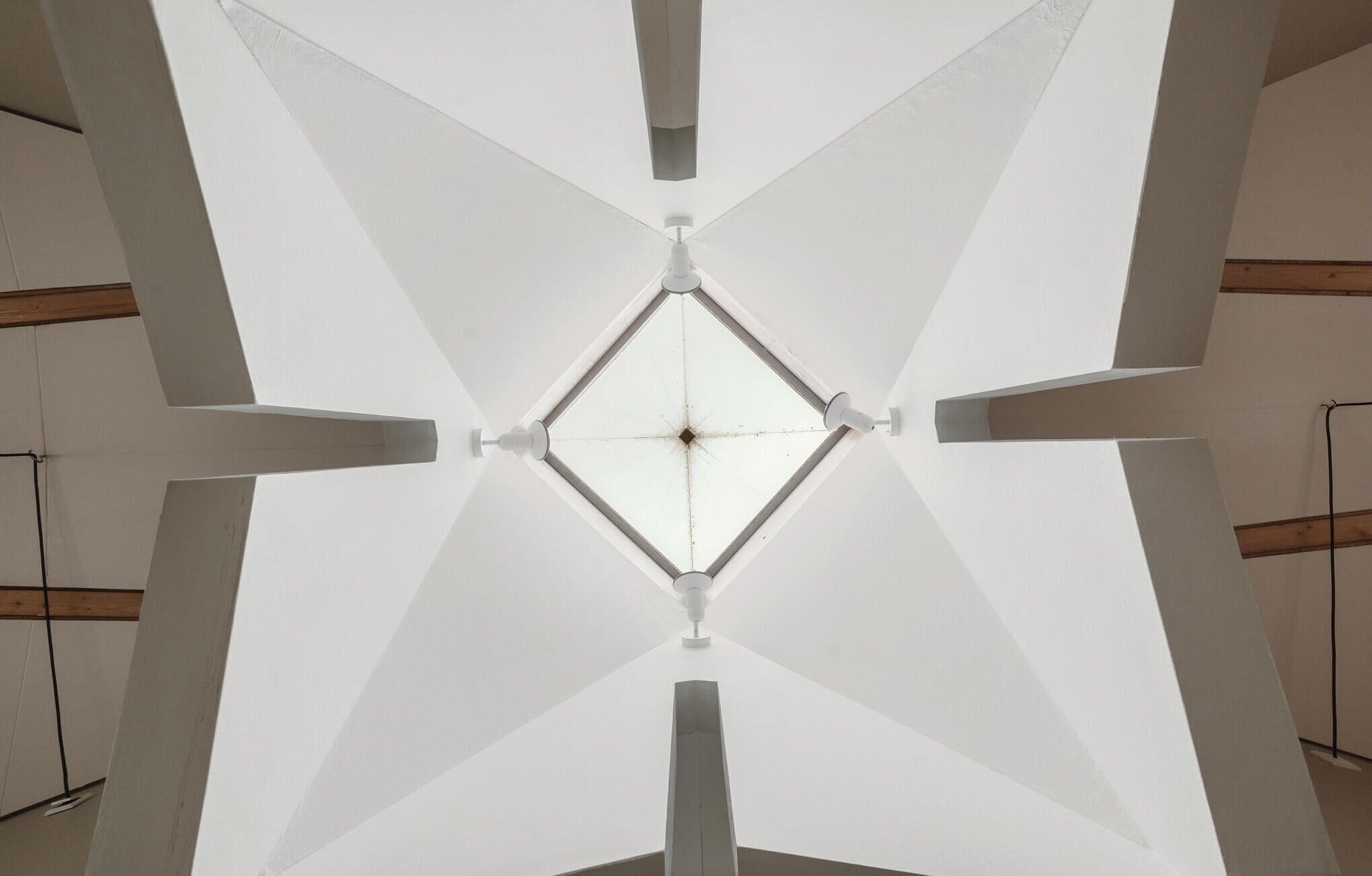 A symmetrical ceiling with a central light fixture and four supporting beams.