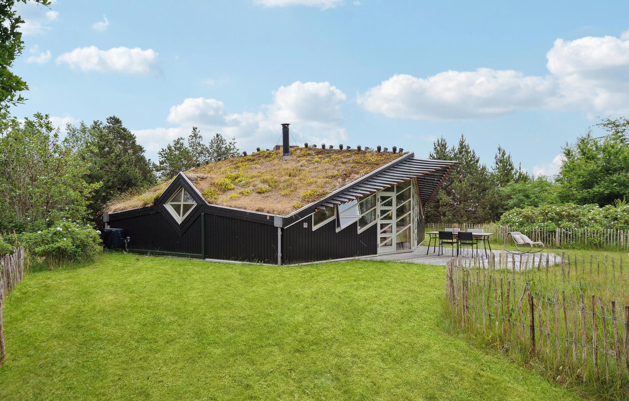 Une maison moderne avec un toit en pente, une grande fenêtre et une terrasse en bois.