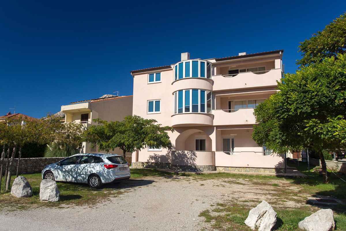Un immeuble à plusieurs étages doté d’une façade incurvée, une voiture garée et une allée gravillonnée.