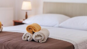 Een net opgemaakt bed met een bruine deken, twee opgerolde handdoeken (een bruin, een wit) en een lamp op een nachtkastje.