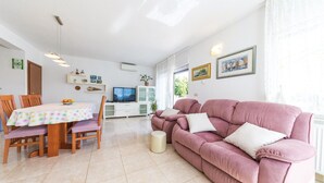 Een woonkamer met een roze bank, een eettafel met stoelen, een televisie en een kast.