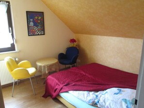 A bedroom with a bed, a desk, two chairs, and a radiator.