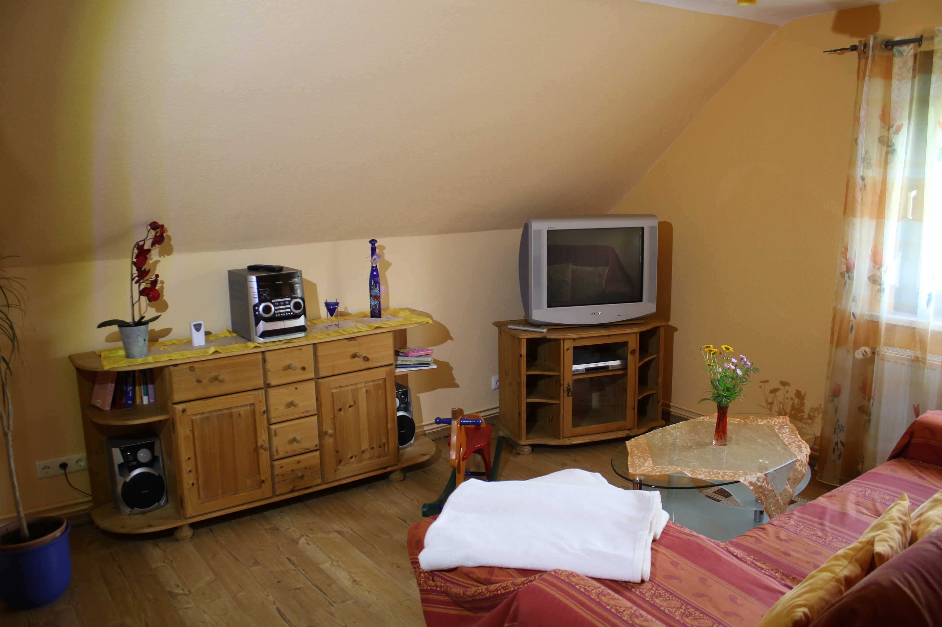 Une pièce comprenant un meuble en bois, une télévision, une petite table avec un vase et un lit recouvert d’une couverture rouge.