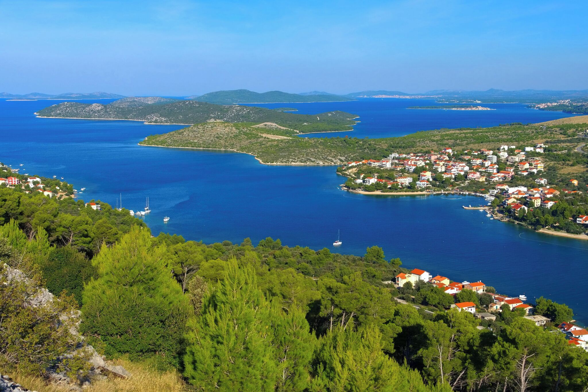 Une ville côtière dotée d’un port de plaisance, entourée de collines verdoyantes et bordée d’eaux d’un bleu limpide.