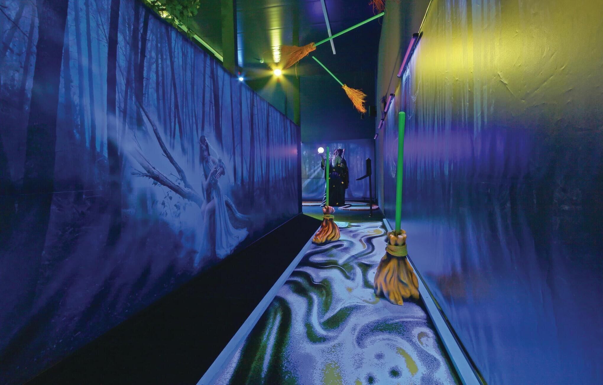 A corridor with a patterned floor, a person in the distance, and a broom leaning against the wall.