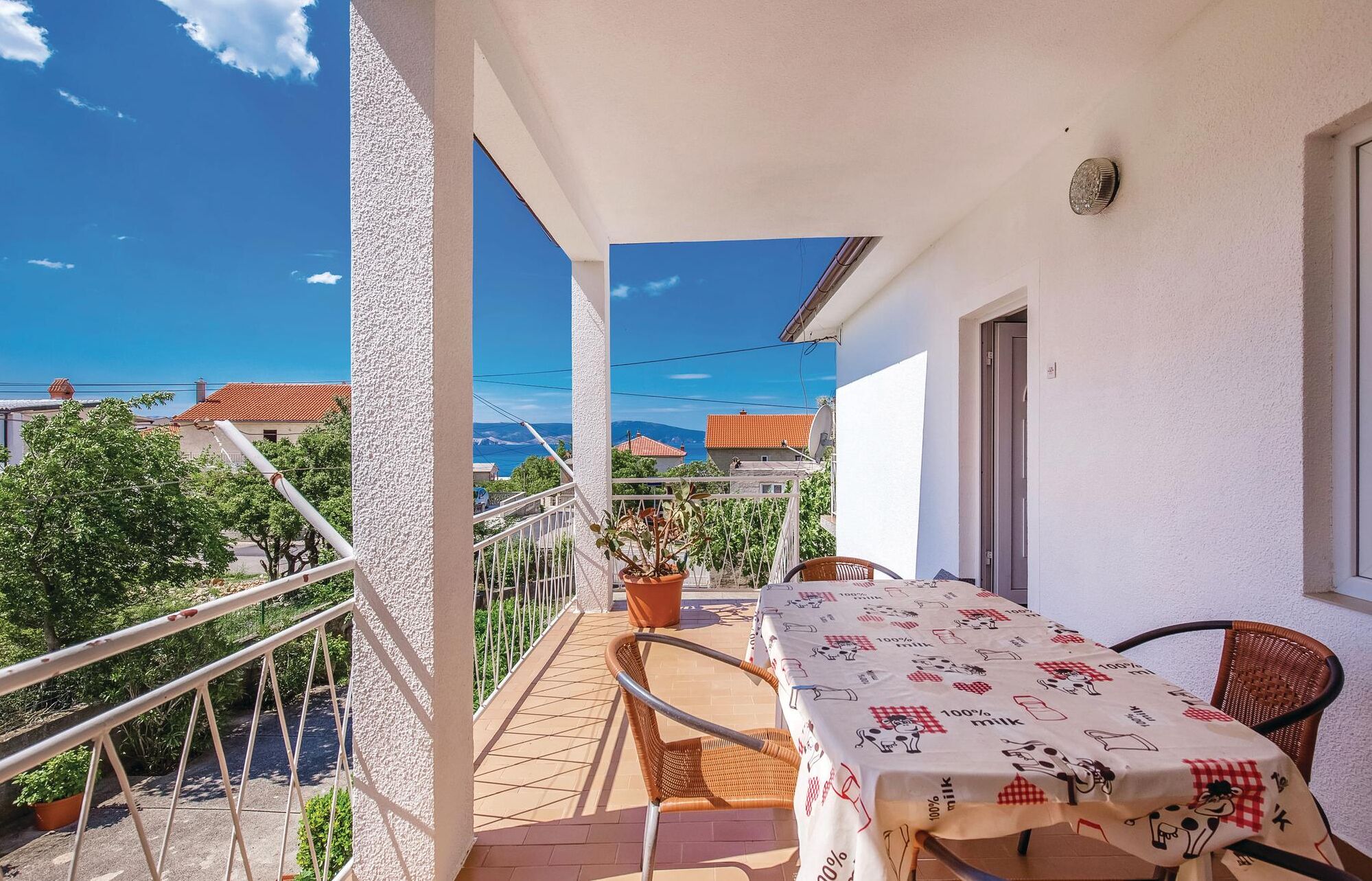 A balcony with a table and chairs, potted plants, and a view of the sea and buildings.