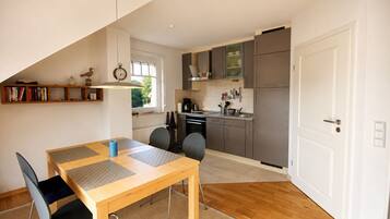 A modern kitchen with grey cabinets, a wooden dining table with chairs, and a built-in bookshelf.