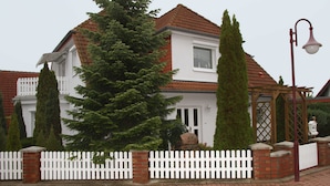 Une maison à deux étages, avec un toit recouvert de tuiles rouges, des murs extérieurs blancs et une clôture blanche en bois.