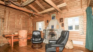 A log cabin interior with a stone fireplace, leather chairs, a wooden table, and a view of the outdoors through a window. - 2 bedroom beautiful home in Balestrand (Balestrand)