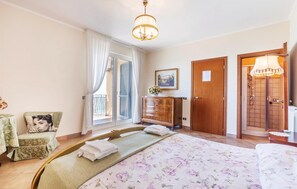 A hotel room with a bed, a wooden dresser, a chair, a window with curtains, and a shower area.