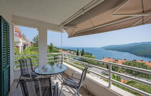A balcony with a round table and chairs, overlooking a coastal landscape with buildings and trees. - Lovely apartment in Rabac with house sea view (Rabac)