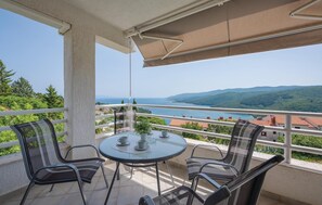 Un balcón con una mesa redonda y sillas, con vistas a la costa, casas y vegetación.