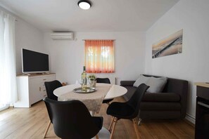 A modern living room with a dining table, black chairs, a sofa, a flat-screen TV, and a painting on the wall. - Holiday apartment with balcony and air conditioning (Čižići)