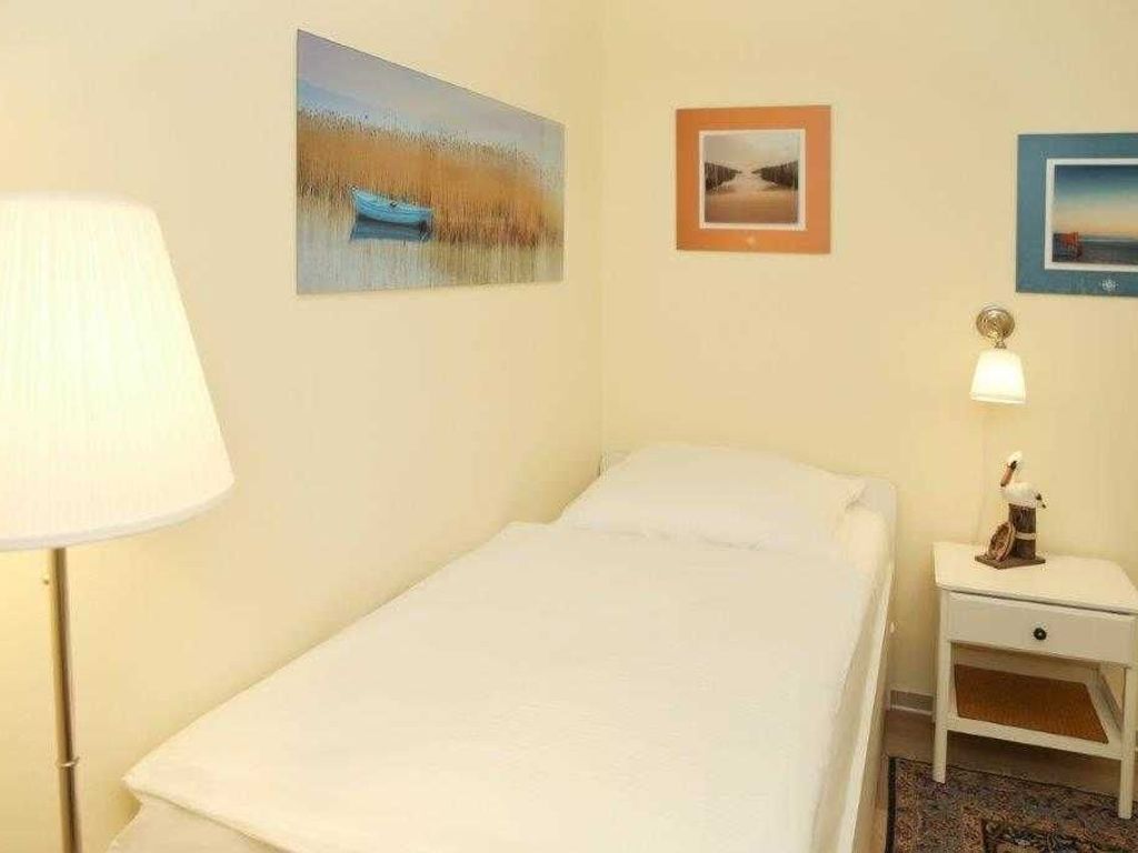 Una habitación de hotel con cama, una mesita de noche con lámpara y tres cuadros en la pared.