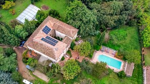 Vue aérienne d’une maison dotée d’une piscine, de panneaux solaires et d’une serre.
