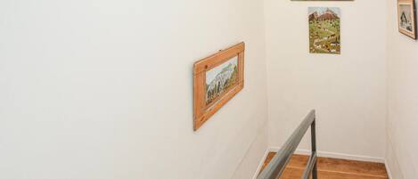 A staircase with wooden steps and a metal handrail, flanked by white walls with framed artwork.
