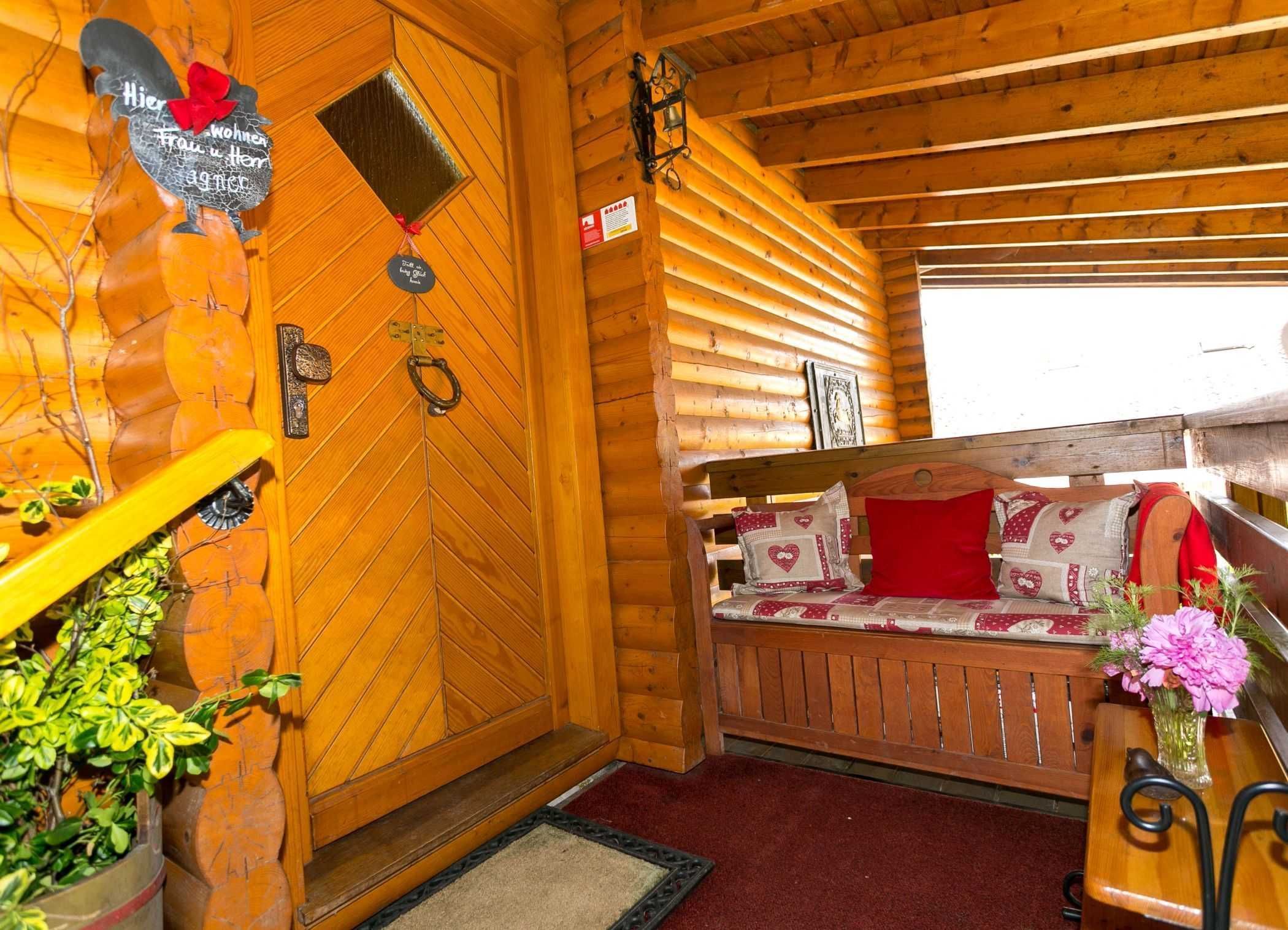 Un acogedor interior de cabaña con una puerta de madera, un banco con cojines y una pequeña mesa con un jarrón de flores.