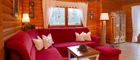 Interior de una cabaña de troncos con un sofá rojo, una mesa de centro de madera y un candelabro.