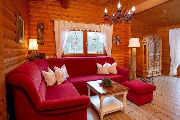A log cabin interior with a red sofa, a wooden coffee table, and a chandelier.