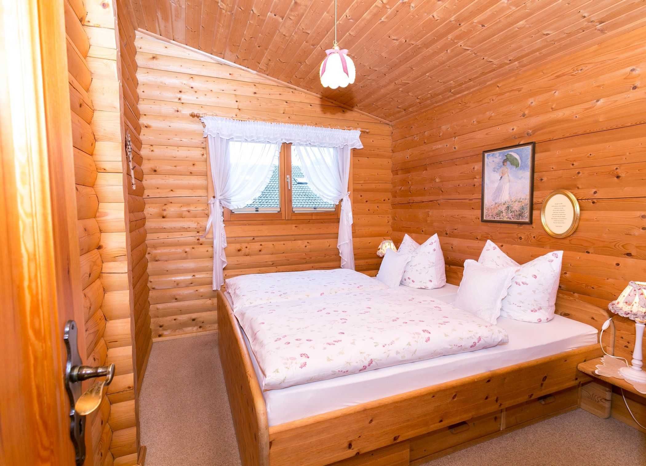 Un dormitorio de cabaña de madera con una cama, cortinas, un cuadro enmarcado y una lámpara de noche.