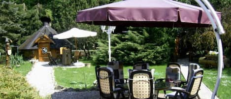 Une terrasse avec une table et des chaises, une pergola surmontée d’une tonnelle, et un chalet en bois en arrière-plan.