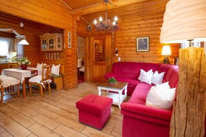 A log cabin interior with a dining area, a red sofa, and a chandelier. - Apartment 1 - Apartments Am Kupferberg (Walkenried)