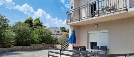 A two-story building with a balcony, outdoor seating, and a stone wall.