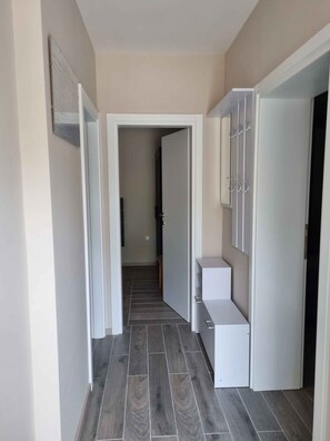 Een gang met een betegelde vloer, witte muren en een deur naar een andere kamer.