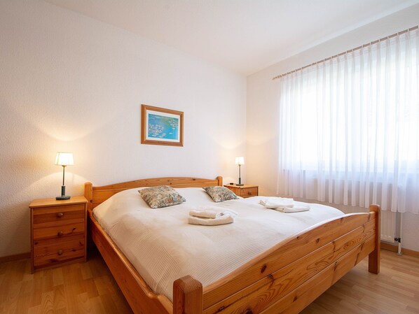 A neatly made bed with a wooden headboard, two bedside tables with lamps, a framed picture on the wall, and a window with sheer curtains. - Reriker Straße RER20-03. - Reriker Straße 20 Whg. 03 (Kühlungsborn)