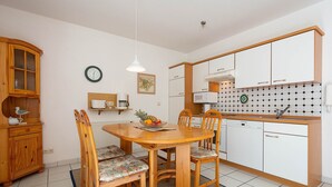 Une cuisine compacte avec un coin repas, des placards en bois, un four à micro-ondes et une horloge au mur.