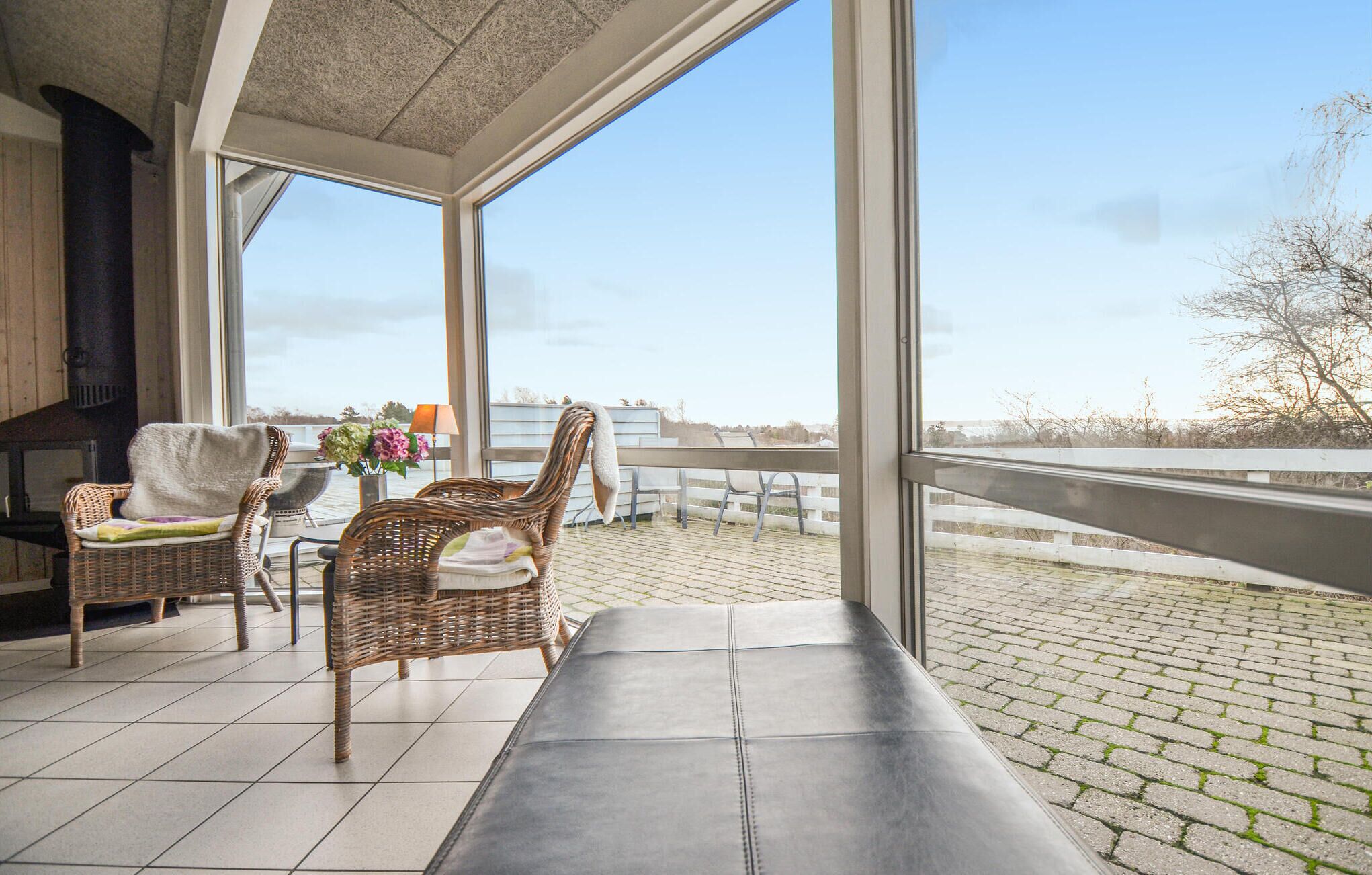 Ein Balkon mit Korbstühlen, einer Bank und Blick auf ein Gewässer.