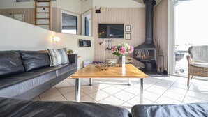 En stue med sofa, sofabord i træ, fjernsyn, pejs og en balkon.