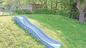 A blue slide in a grassy area with trees and a stone wall in the background. - 5 bedroom stunning home in Fredericia (Fredericia)