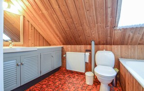 Un baño pequeño con paneles de madera, suelo de baldosas rojas, inodoro blanco, lavabo y radiador.
