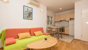 A compact living space with a sofa, a small round table, a kitchen area with a fridge, oven, and bar stools. - 2 bedroom beach front apartment in Makarska (Makarska)