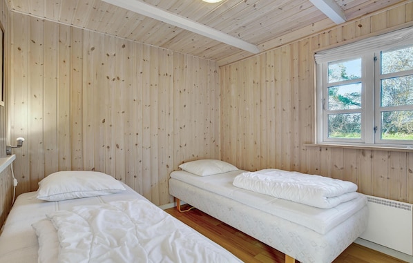 Une pièce aux murs en bois et une fenêtre donnant sur les arbres. On y trouve deux lits avec du linge de lit blanc.
