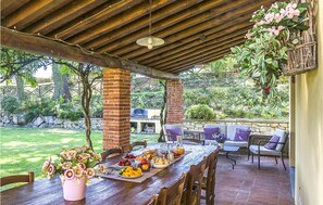 Eine Terrasse im Freien mit einem Holztisch, gedeckt für eine Mahlzeit, umgeben von Stühlen und einer gepolsterten Sitzecke.