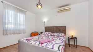 Un dormitorio con cama, mesita de noche, lámpara, ventana con cortinas y unidad de aire acondicionado.