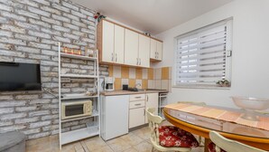 Cocina compacta con pared de ladrillo, armarios blancos, microondas y comedor con mesa y sillas.
