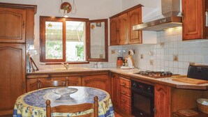 Een keuken met houten kastjes, een fornuis, een spoelbak en een raam met uitzicht op groen.