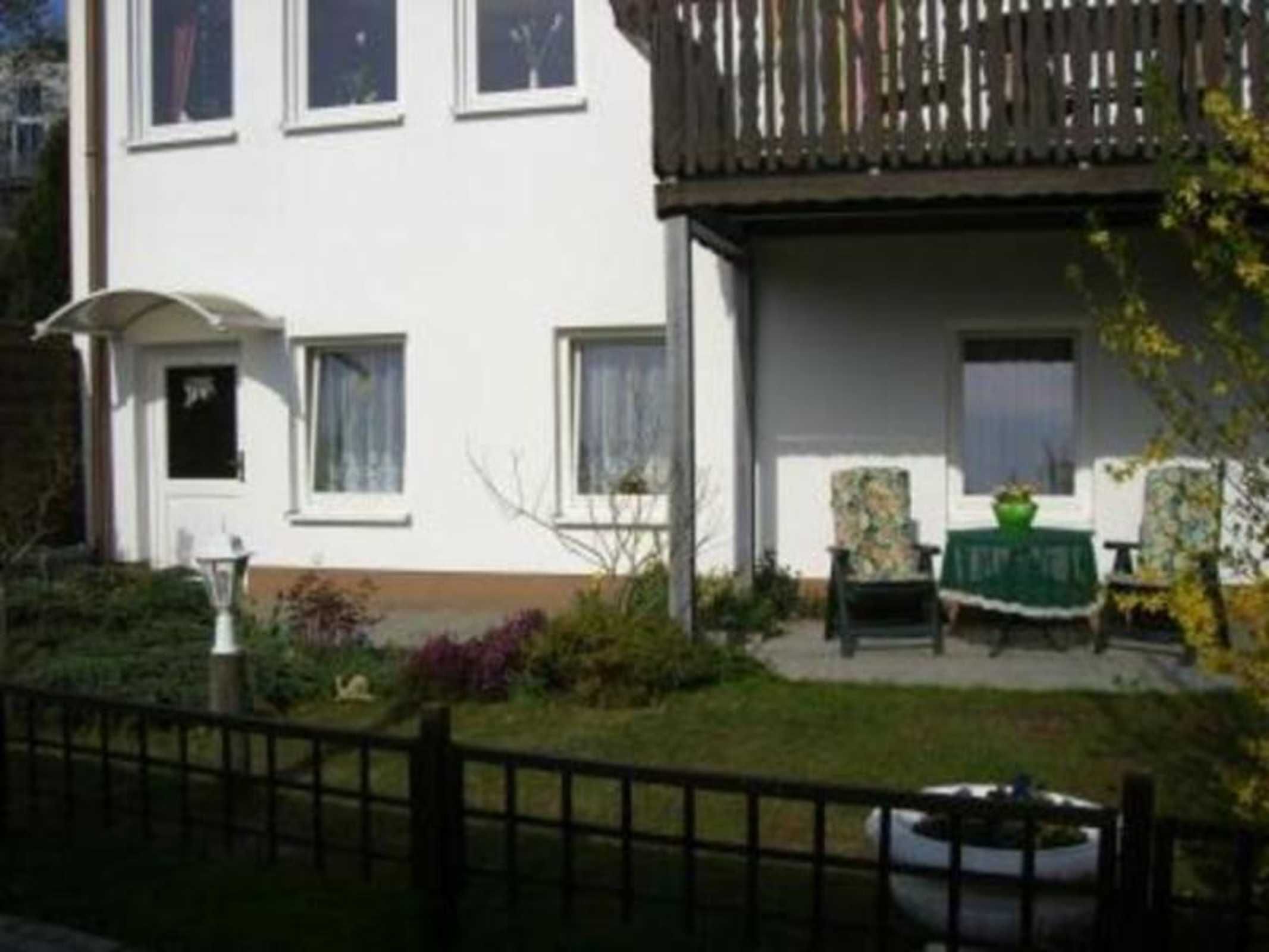 Un edificio a due piani con un balcone, un piccolo giardino e un tavolo con sedie.
