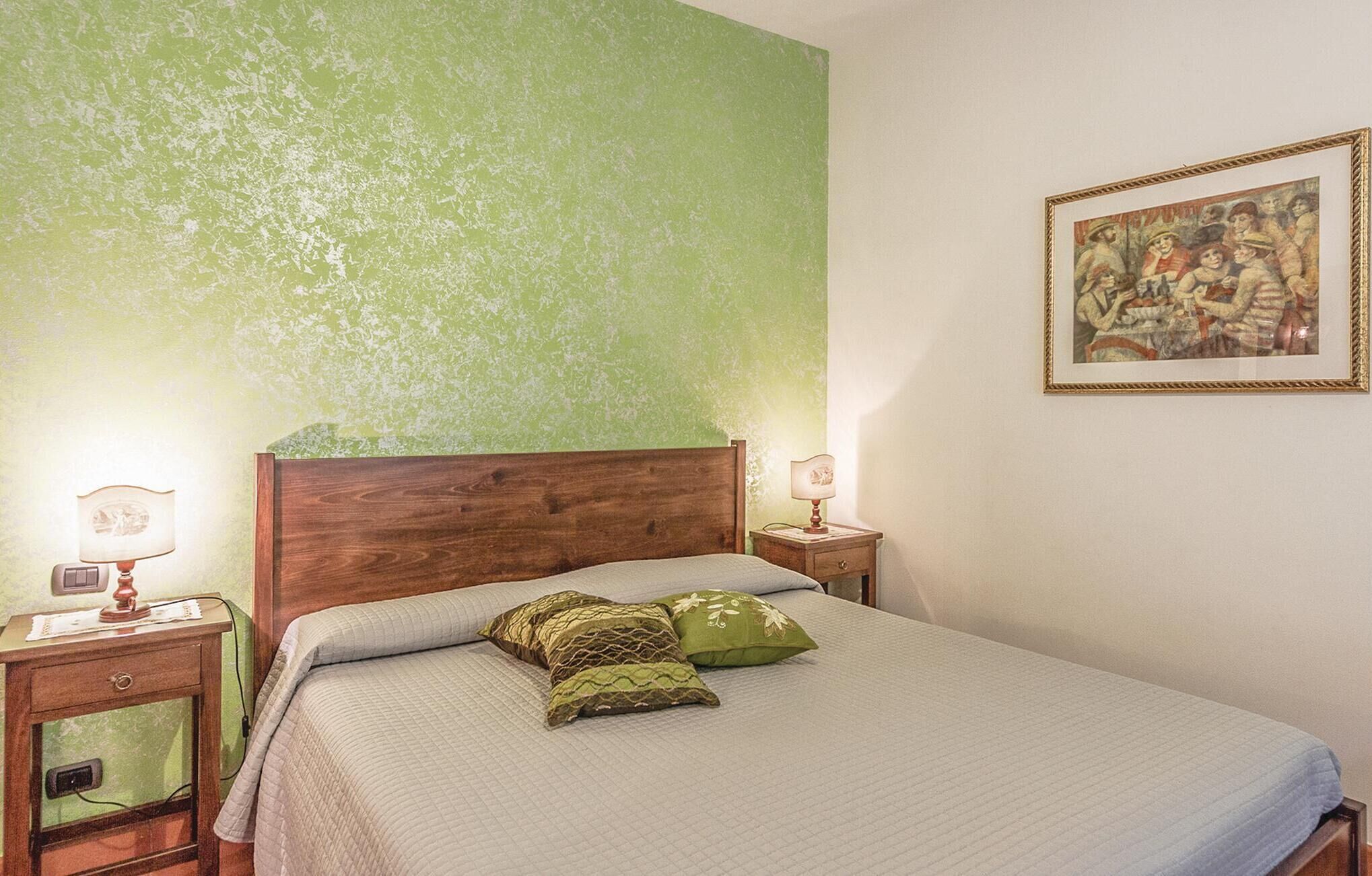 A bedroom with a wooden bed, green textured walls, and a framed painting on the wall.